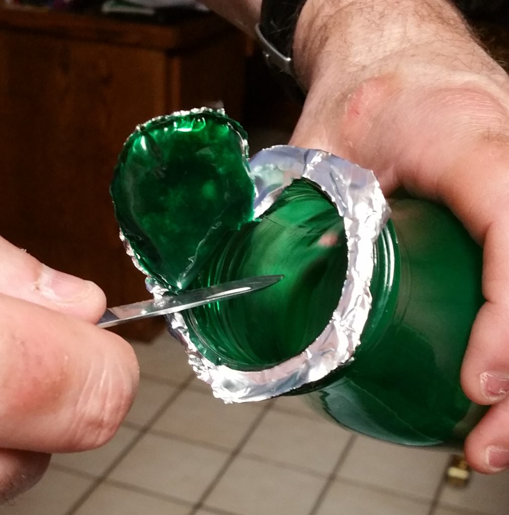 A handy dandy pocket knife being put to use to more cleanly remove the foil without removing as much of the glue from the bottle.